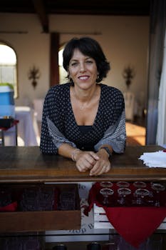 Portrait of a smiling woman standing behind a wooden bar counter in an indoor setting.