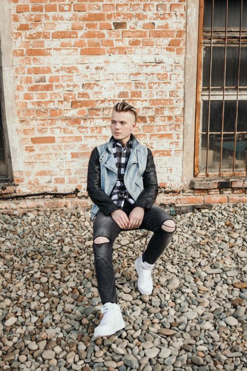 Free Stylish young man with unique hairstyle sitting against a rustic brick wall, exuding individuality and fashion-forward style. Stock Photo
