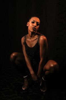Black woman in a glittering bodysuit posing elegantly in a studio setting.