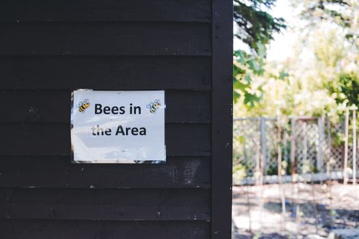A black wall with a warning sign about bees in the area, surrounded by greenery.