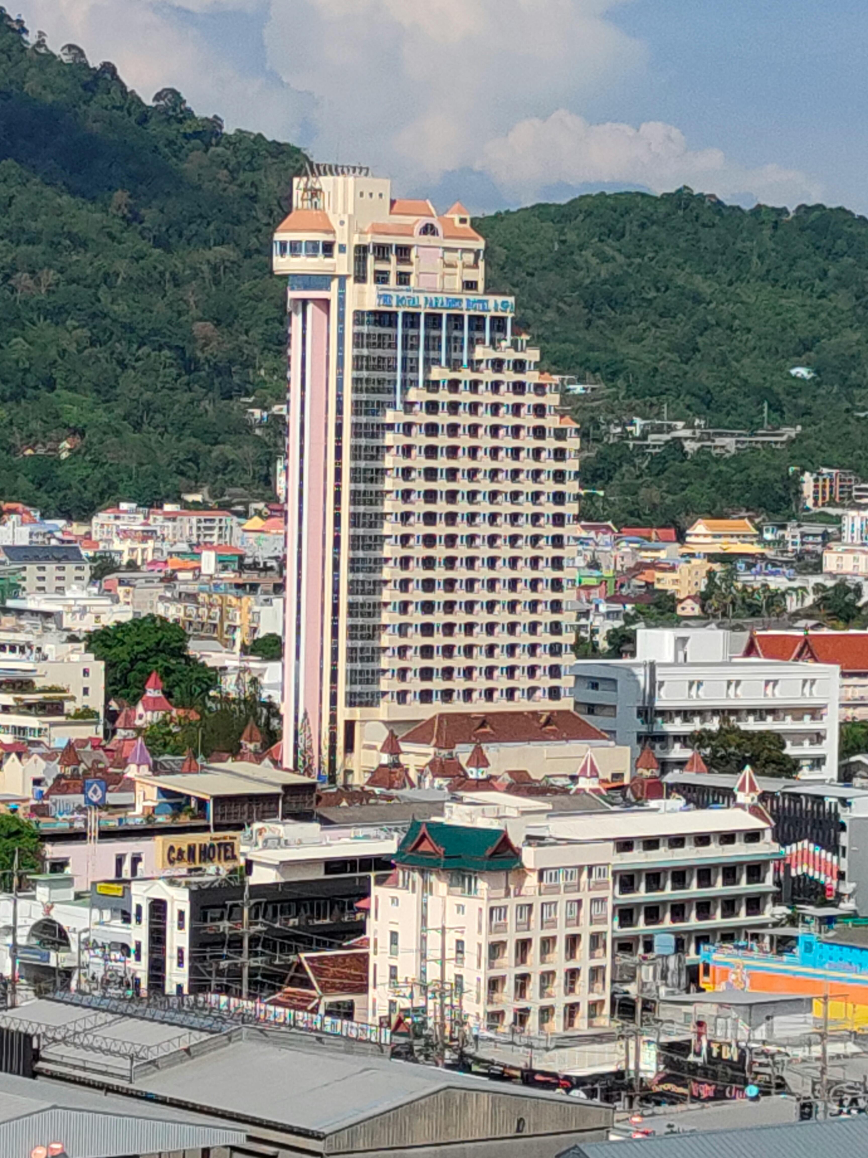 Free High-rise hotel with modern architecture in Patong, Phuket with lush green mountains in the background. Stock Photo