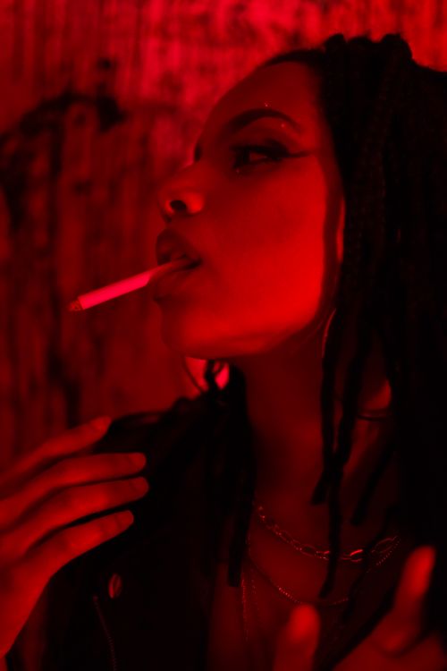 Free Close-up portrait of a woman smoking under dramatic red lighting. Stock Photo