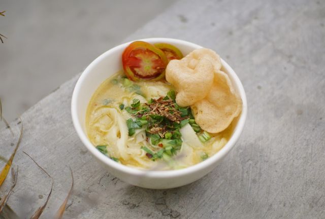 A bowl of traditional Indonesian soto ayam with fresh vegetables and crackers, perfect for a savory meal.