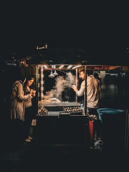 A bustling nighttime street food stall with a vendor and customers enjoying the warm atmosphere.
