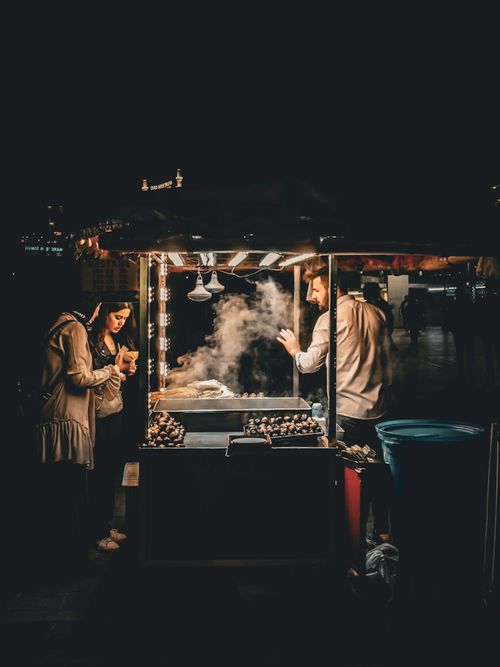 Free A bustling nighttime street food stall with a vendor and customers enjoying the warm atmosphere. Stock Photo