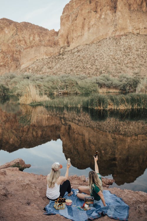 Two Woman Sitting on Blue Blanket Facing Rock Cliff