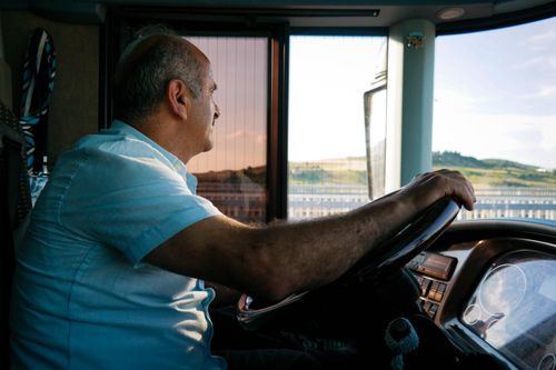 Free An elderly man driving at sunset, enjoying the view as he navigates the road. Stock Photo