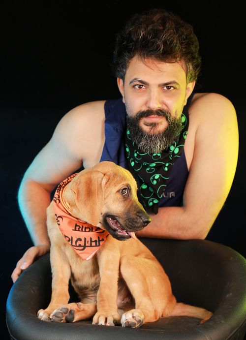 Free Portrait of a bearded man and puppy in a studio with a dark background and colorful lighting. Stock Photo