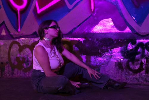 Free A fashionable woman in sunglasses poses against neon-lit graffiti in Ciudad de México. Stock Photo