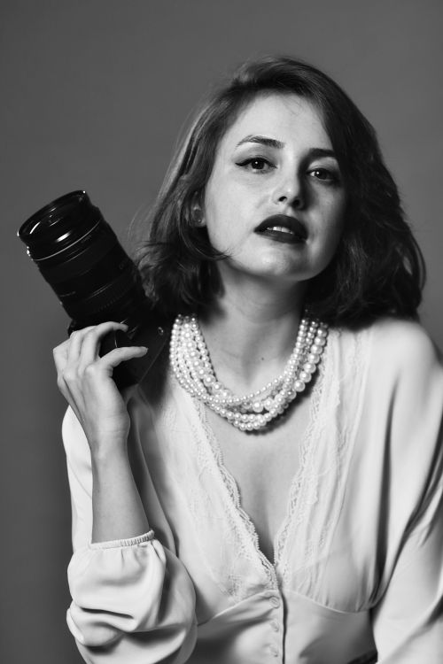 Free Black and white portrait of a woman in a pearl necklace, holding a camera. Stock Photo