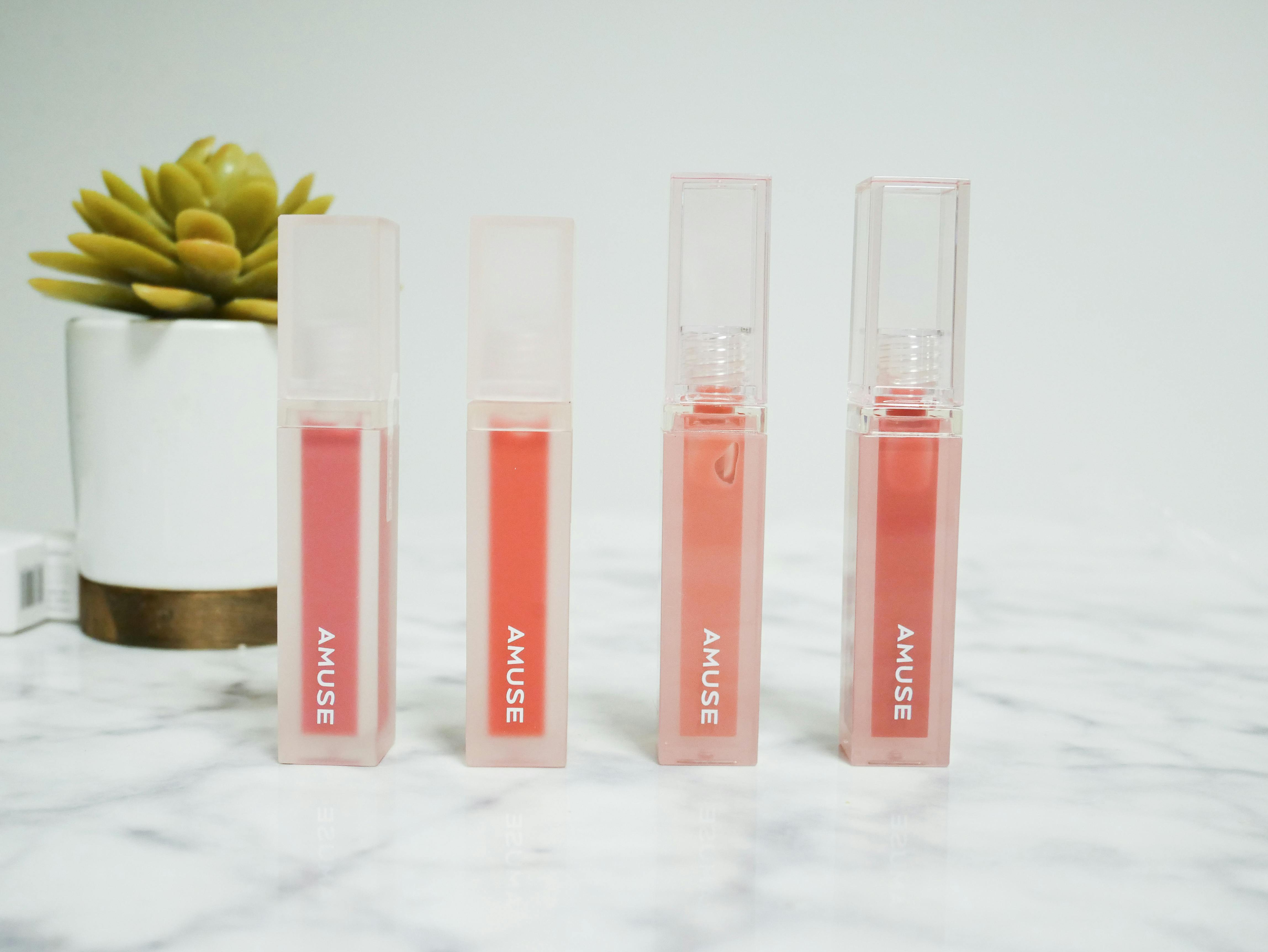 Elegant display of lipsticks in clear packaging with succulent on a marble surface.