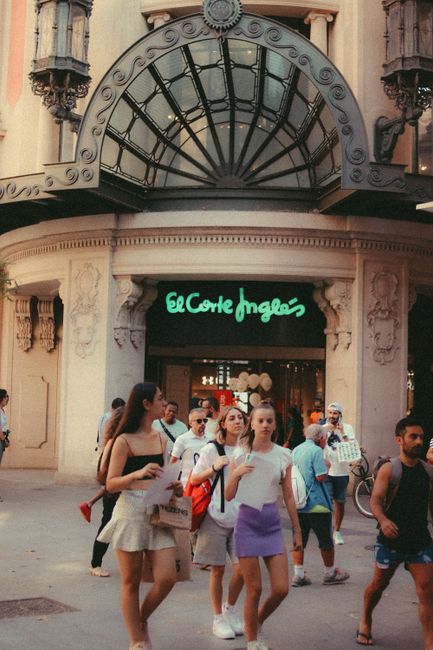 Fotomural Peatones fuera de la entrada de El Corte Inglés con una fachada ornamentada en un entorno urbano.