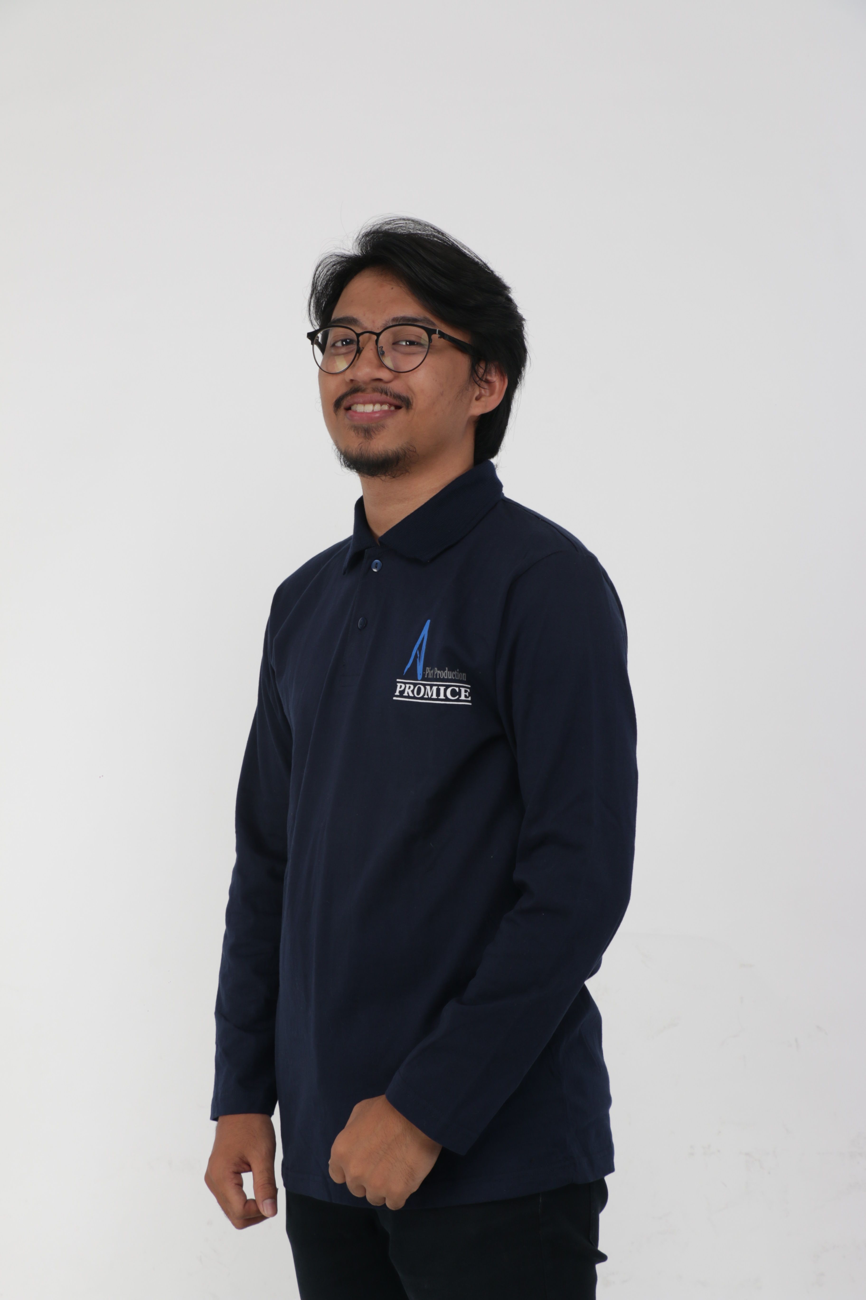 Asian man smiling in a dark blue long-sleeve shirt with a logo, against a white background.