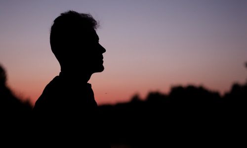 Free Silhouette of a person against a colorful sunset sky, creating a serene outdoor scene. Stock Photo