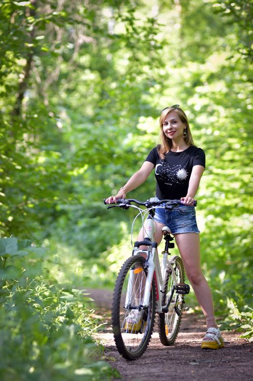 Free Young woman in denim shorts enjoying a bike ride through a lush forest trail. Stock Photo