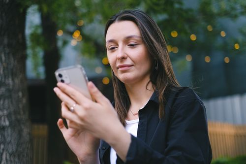 Free A young woman looking at her smartphone with a gentle smile in an outdoor setting, surrounded by nature. Stock Photo