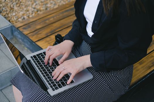 Close-up of woman typing on laptop outdoors wearing a black shirt and polka dot skirt.