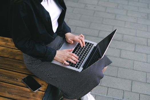 Woman sitting outdoors typing on a laptop, embodying freelance and digital nomad lifestyle.