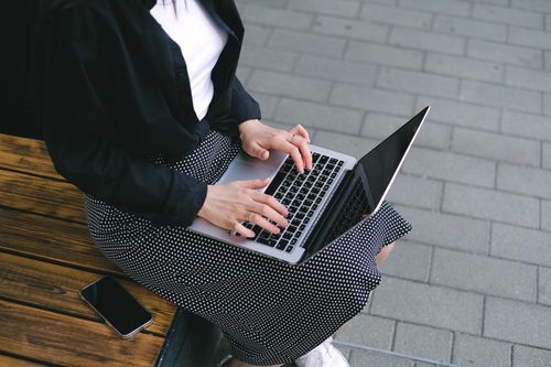 Free Woman sitting outdoors typing on a laptop, embodying freelance and digital nomad lifestyle. Stock Photo