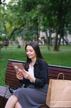 Young woman using a tablet while sitting on a park bench. Relaxed and connected lifestyle.