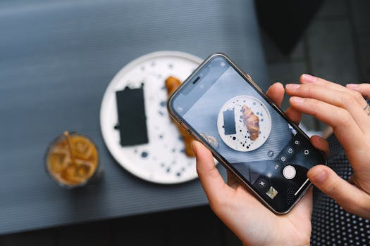 Hands photographing a croissant on a plate with a smartphone, featuring coffee.