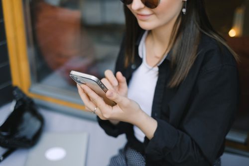 Free A stylish woman using her smartphone while sitting indoors by the window. Stock Photo