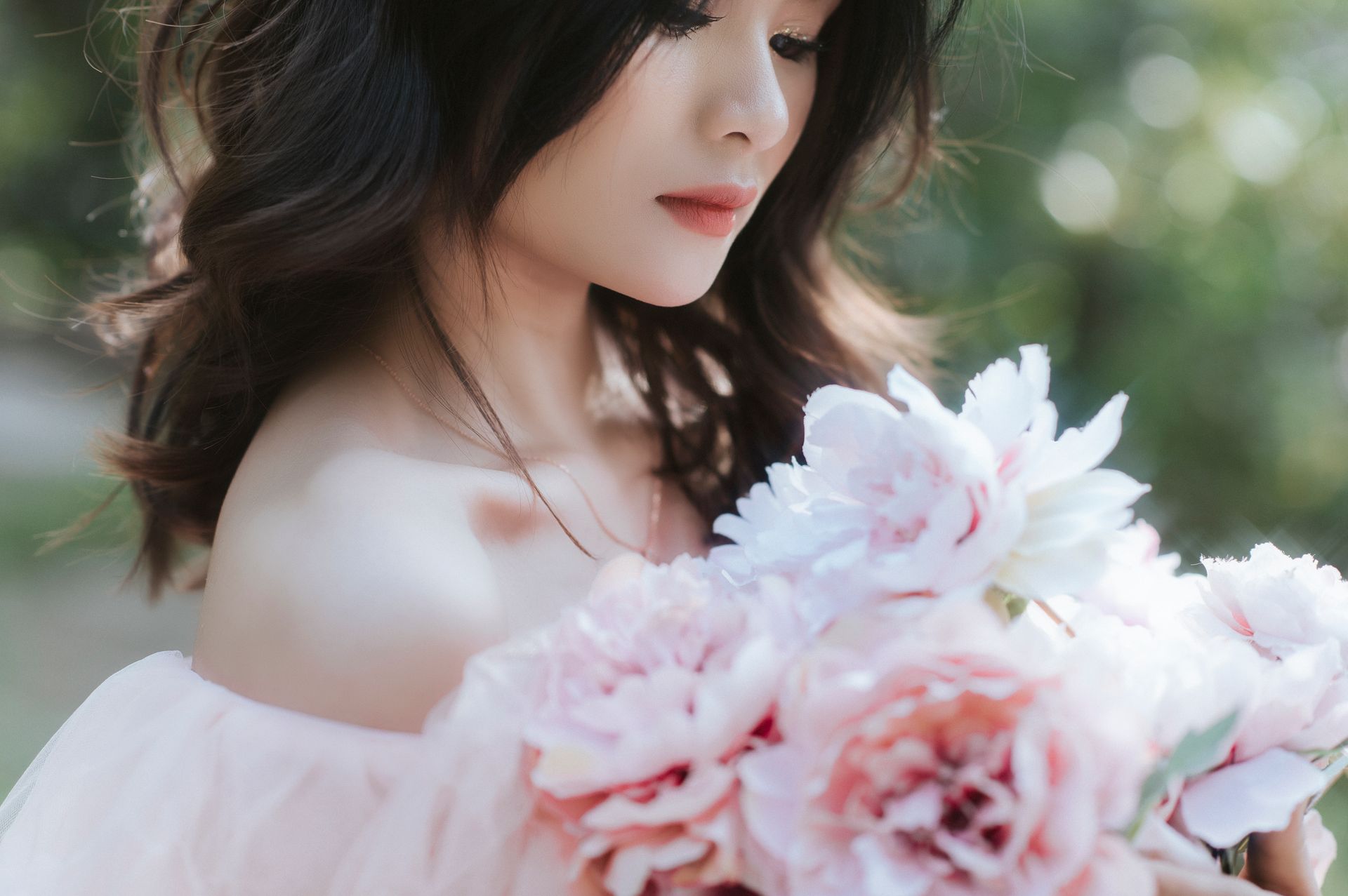 Beautiful woman in a pink dress holding peonies outdoors