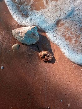 Detailed shot of rocks on sandy beach with sea foam at shoreline, perfect for nature themes.