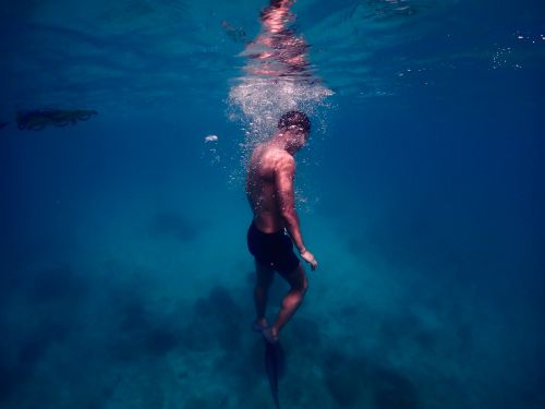 Free A diver explores underwater, surrounded by bubbles and serene ocean blue hues. Stock Photo