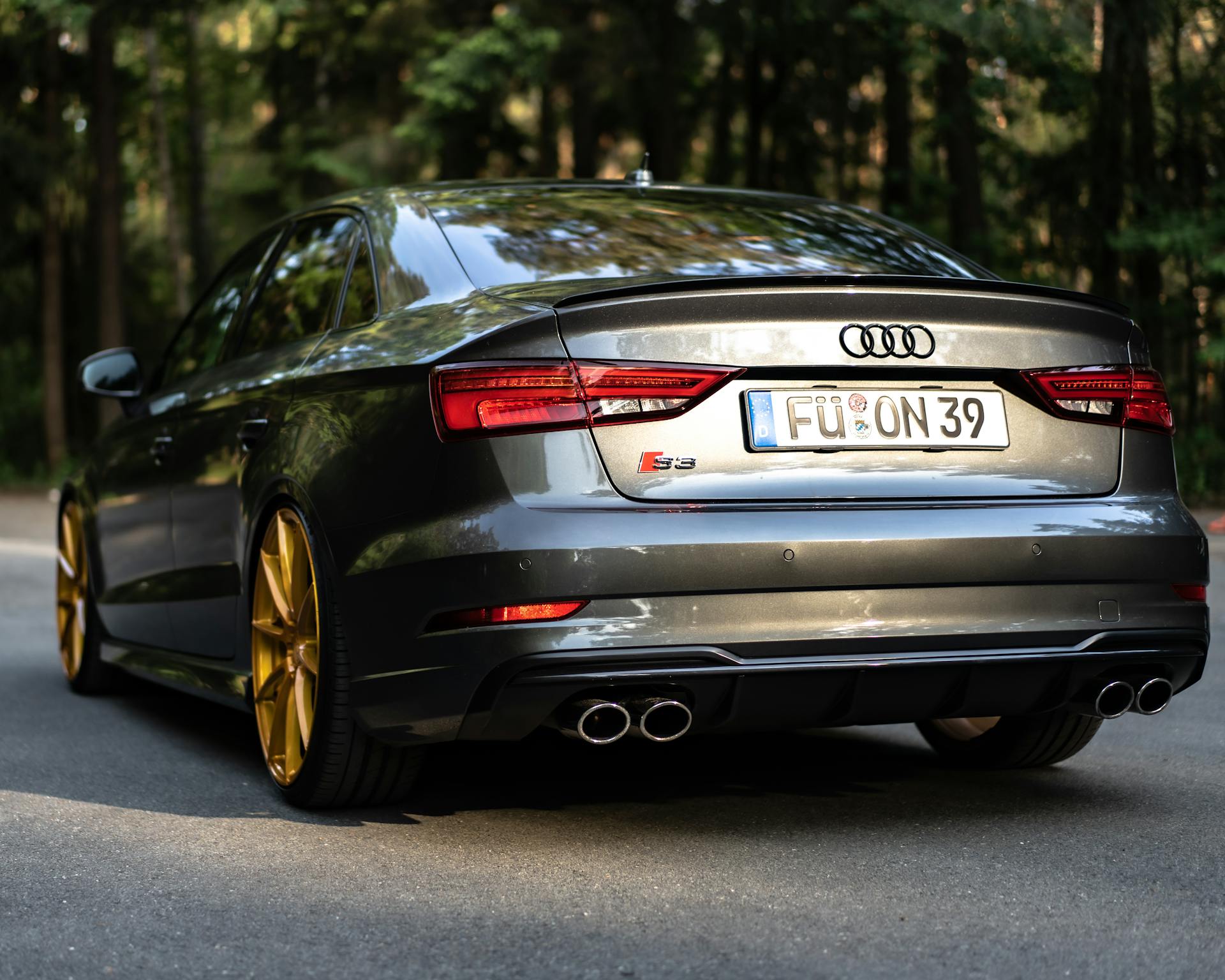 Rear view of a stylish Audi S3 sedan parked on a winding forest road with golden wheels.