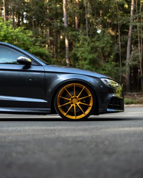 Stylish black sedan with gold rims parked on a serene forest road, showcasing elegance and automotive design.