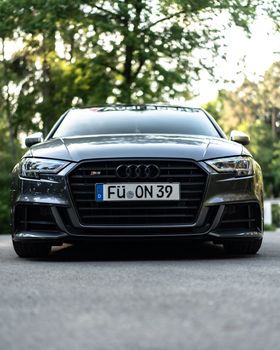 Front view of a luxury Audi S3 parked outdoors on a scenic tree-lined road.