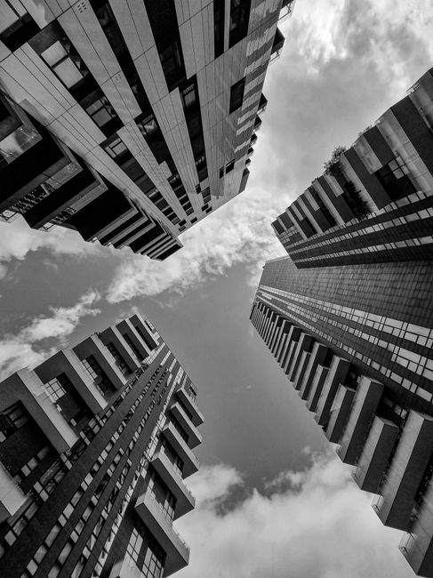 Low-angle view of modern skyscrapers converging towards the sky in grayscale.