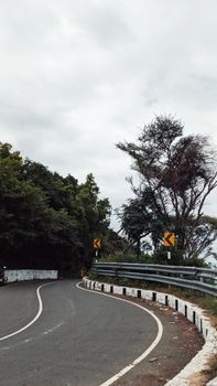 Curvy asphalt road with green trees and a cloudy sky in Chinnaveppambattu, India.