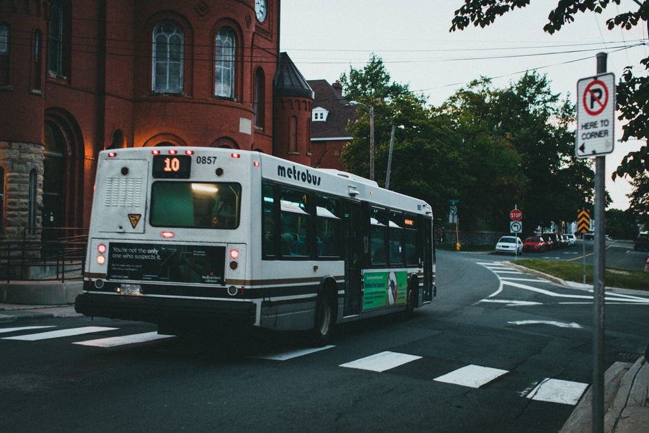 A metrobus rides through urban streets near red brick buildings at dusk, reflecting public transit in a cityscape.
