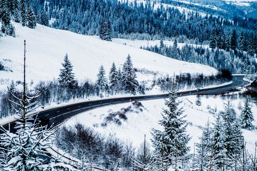 Aerial view of a snowy winding road through a forested winter landscape.