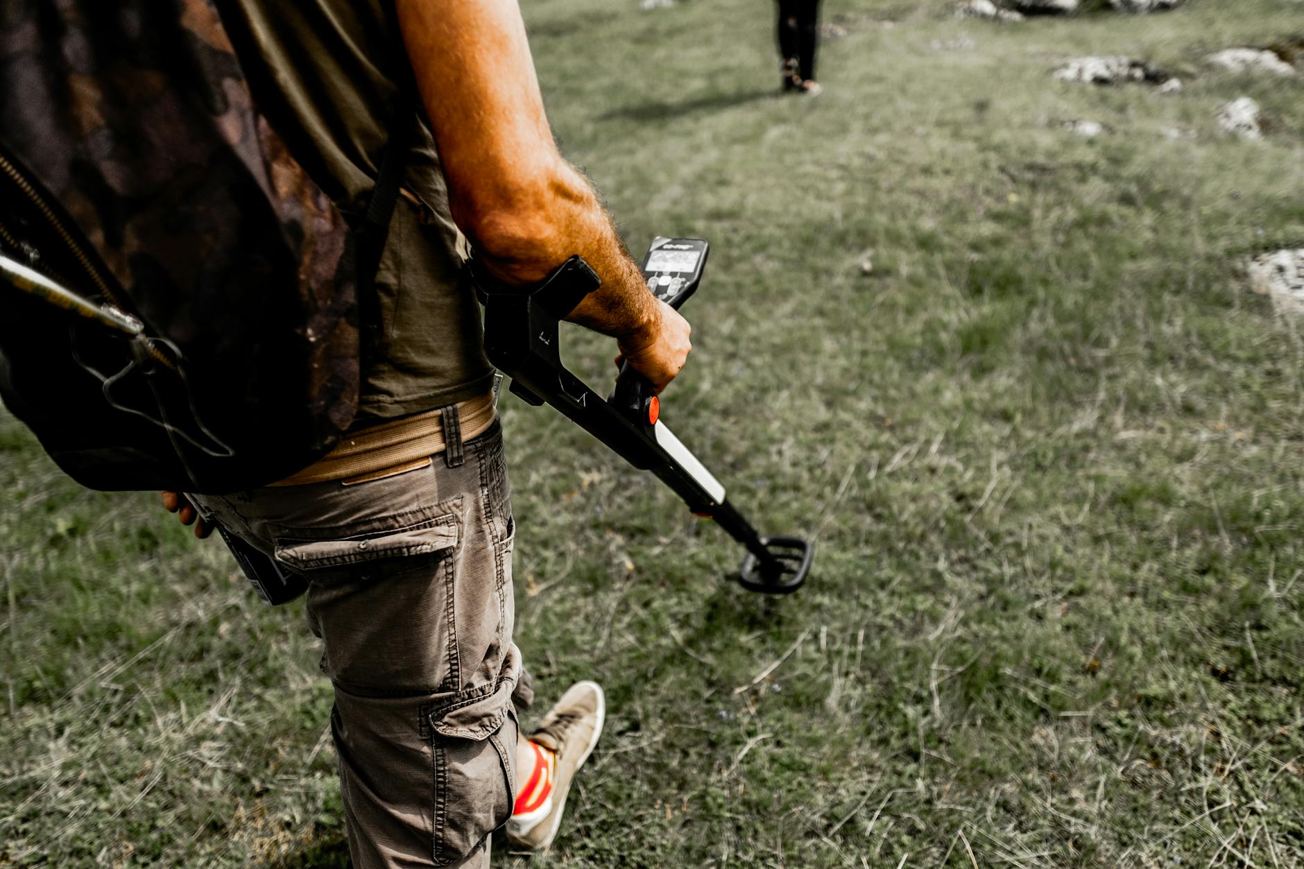 Person using a metal detector on a grassy field wearing casual attire.