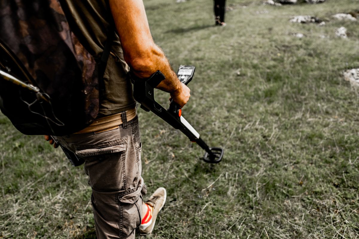Person using a metal detector in a grassy field