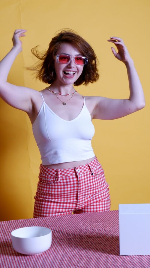 Free Smiling woman in checkered shorts and sunglasses, embracing a joyful moment against a yellow background. Stock Photo
