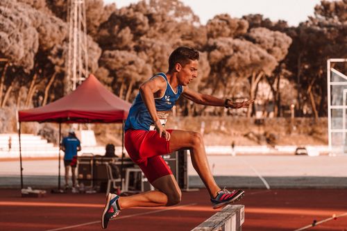 Free Dynamic shot of a young athlete in blue and red jumping a hurdle during a track race. Stock Photo