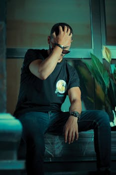Young man in black shirt sitting indoors with a thoughtful pose.