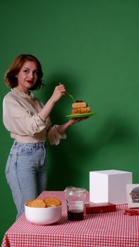 Young woman smiling while holding a plate of pancakes in a studio with a green background.