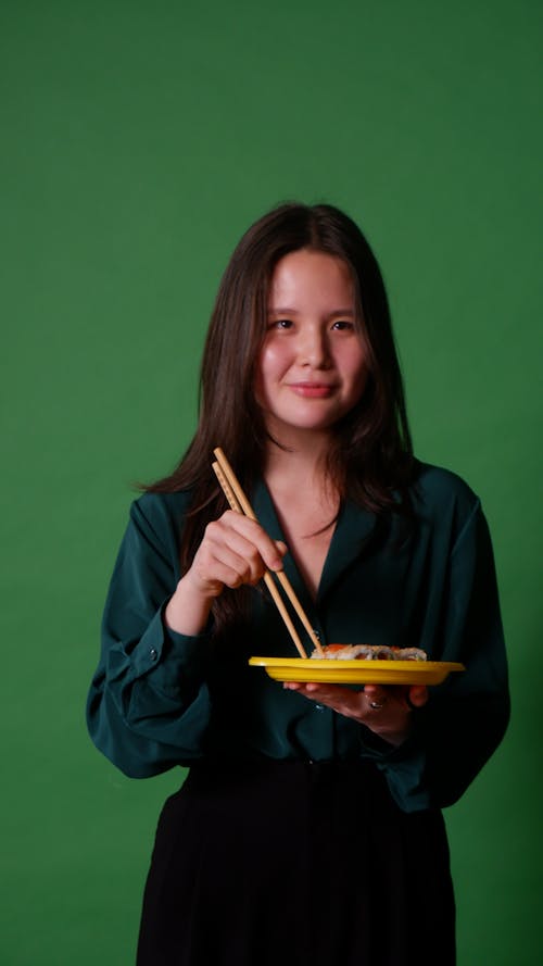 A Woman in Blue Long Sleeve Holding a Yellow Plate and Chopsticks