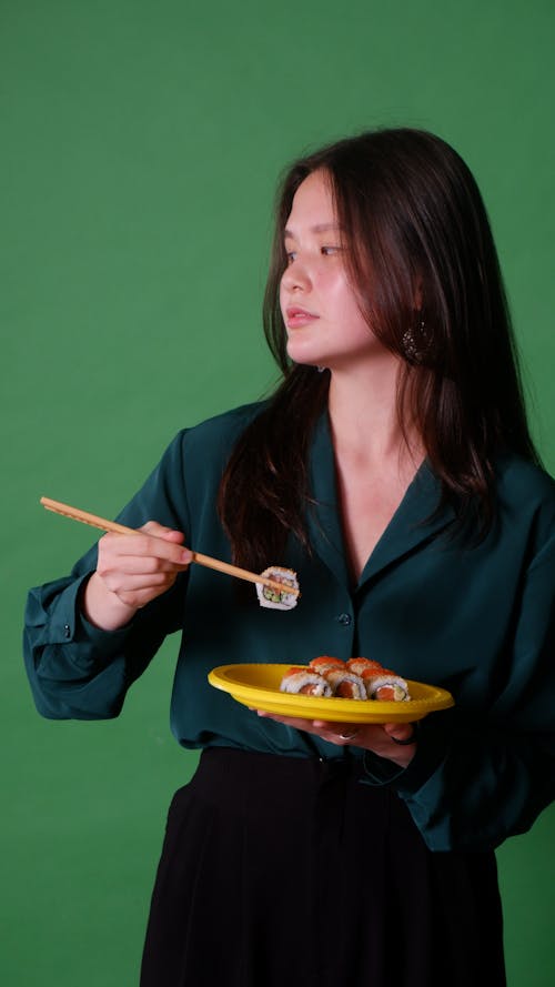 A Woman in Blue Long Sleeves Holding a Chopsticks with Sushi Roll