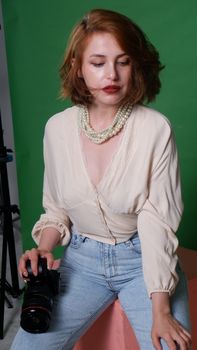 Fashionable woman with camera in bright studio with green backdrop, conveying a modern portrait mood.