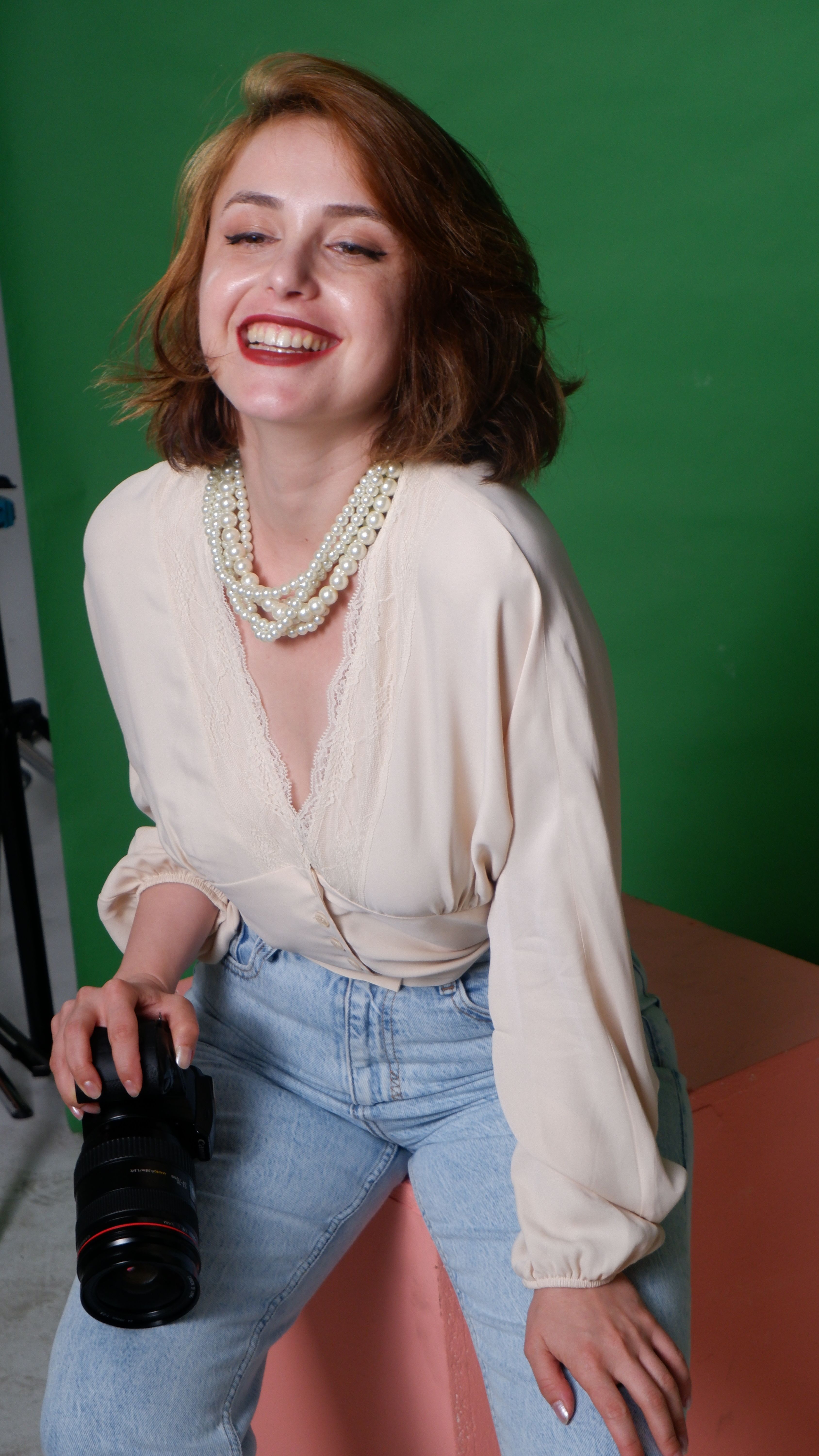 Smiling woman holding a camera, posing joyfully against a green background.