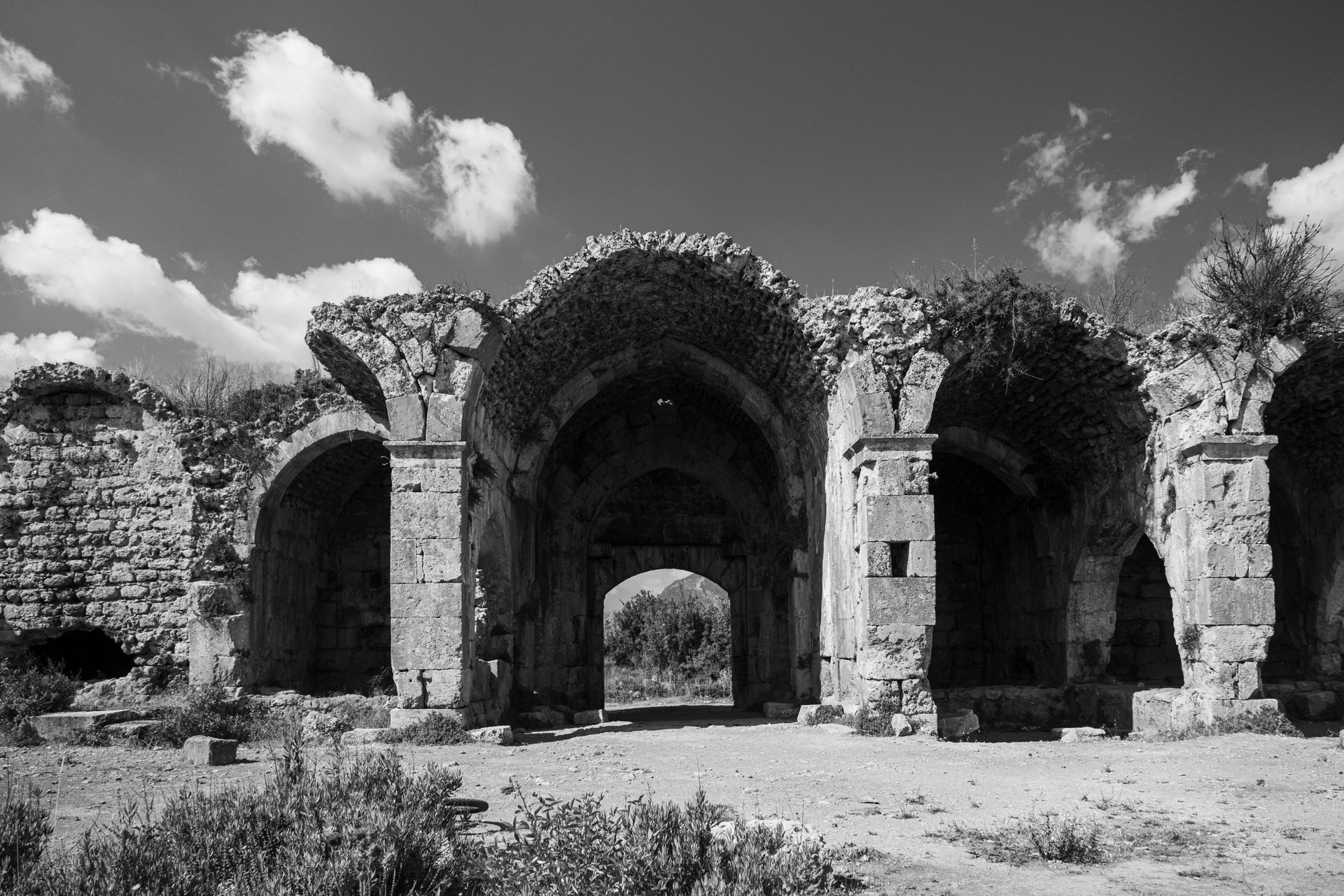 Black and white photo of ancient stone ruins with archway against a cloudy sky.