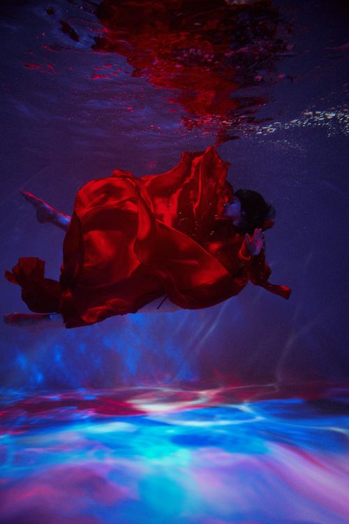 Free A young woman in a red dress gracefully floats underwater, creating a dreamlike scene. Stock Photo