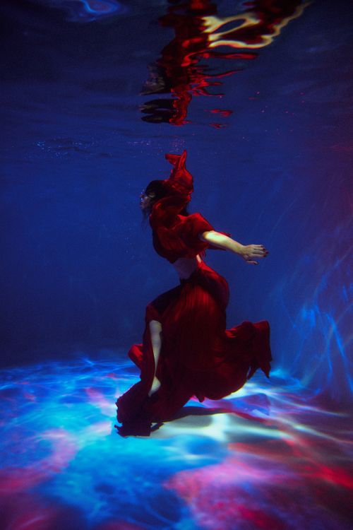 Free A woman gracefully floating underwater in a vibrant red dress. Stock Photo