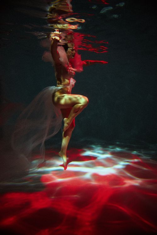 Free A woman gracefully dances underwater, illuminated by red and moody lighting. Captivating reflection effects. Stock Photo